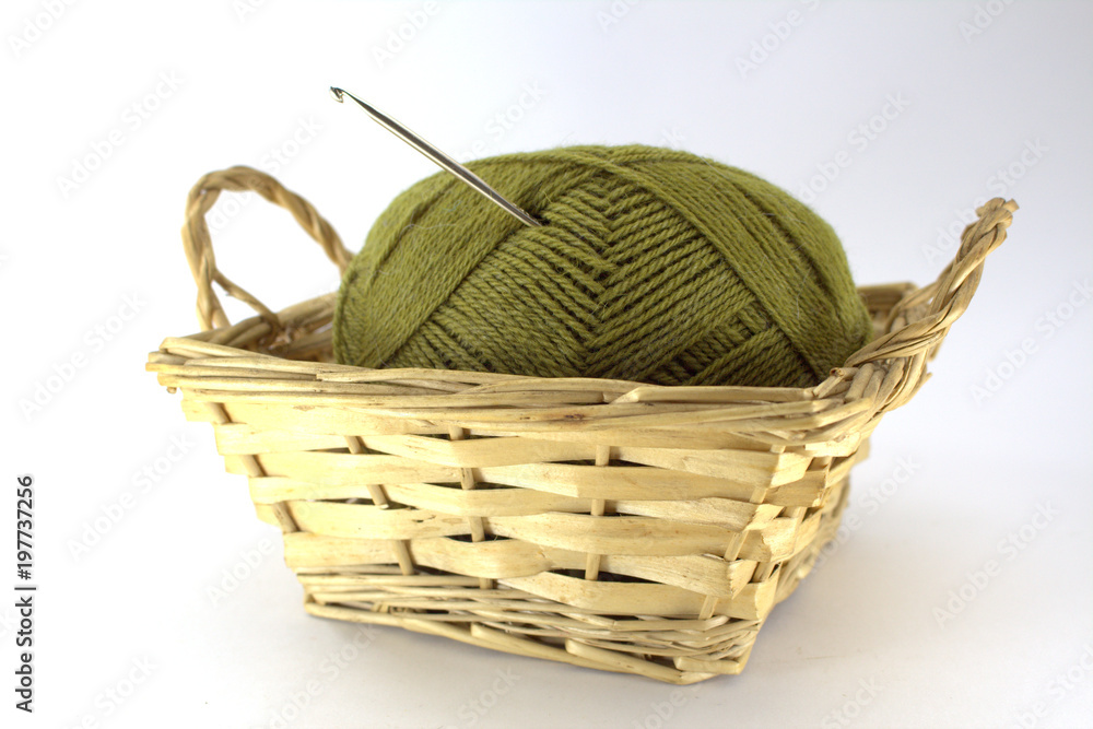 Green tangle of natural wool for needlework with a crocheted crochet stuck in it in a wicker basket on a white background close-up Green tangle of natural wool for needlework with a crocheted crochet stuck in it in a wicker basket on a white background close-up