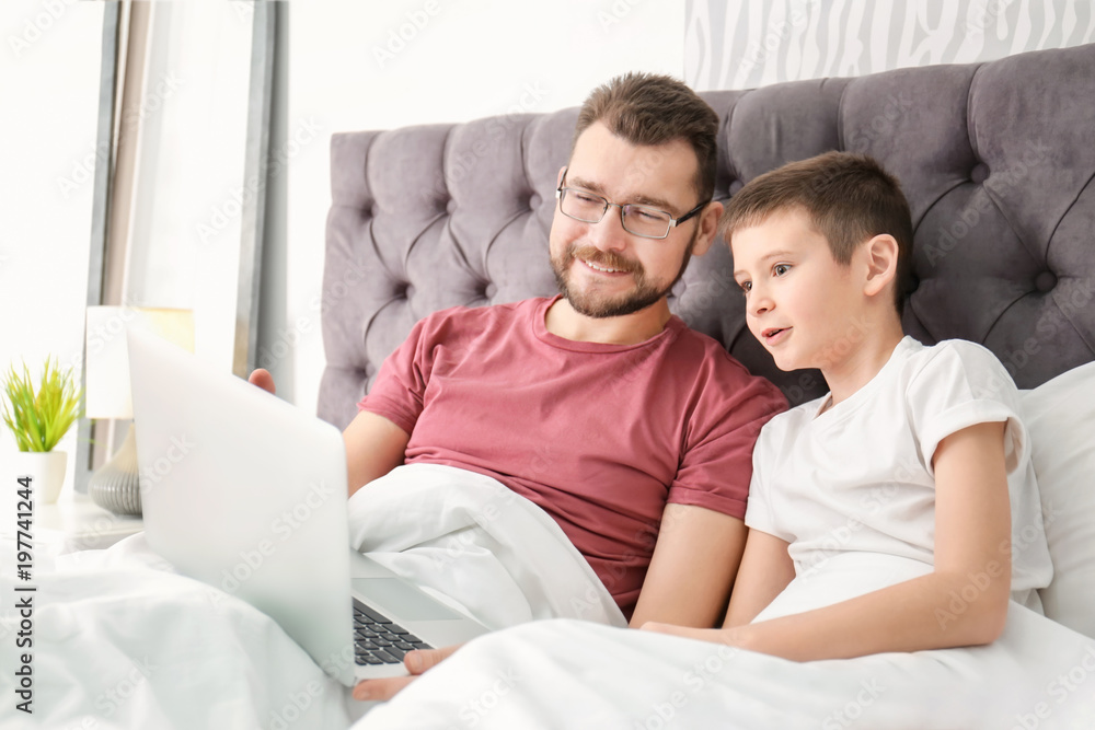 Little boy and his dad using laptop in bedroom Little boy and his dad using laptop in bedroom
