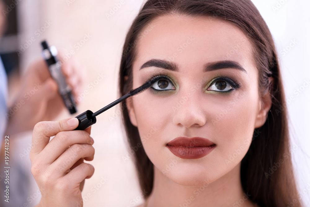 Professional visage artist applying makeup on woman's face in salon, closeup