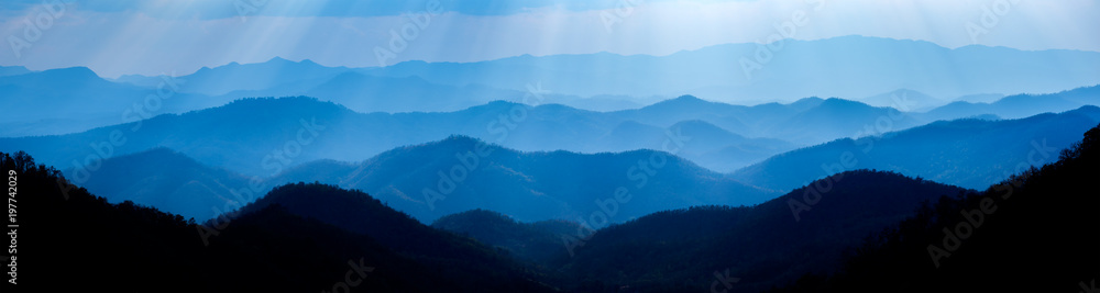 Beautiful landscape of blue mountains layers during sunset with sunrays - obrazy, fototapety, plakaty 
