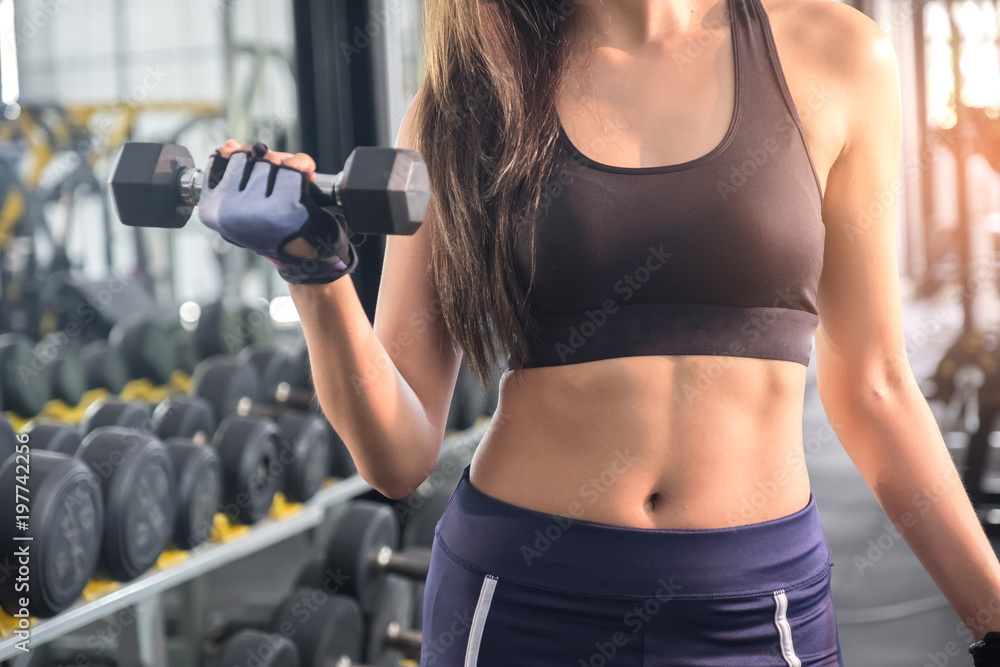 Fitness woman lifting dumbbell in hand.Focus on belly and dumbbell. Fitness woman lifting dumbbell in hand.Focus on belly and dumbbell.