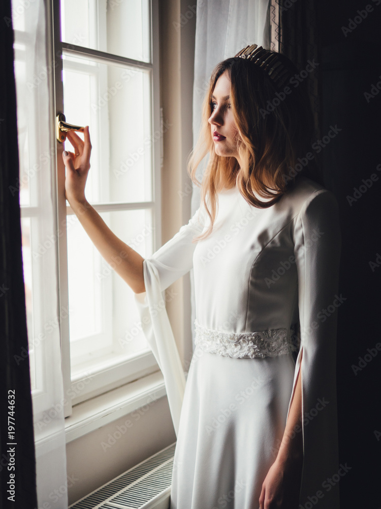 bride near window. white european wedding dress with tiara diadem bride near window. white european wedding dress with tiara diadem