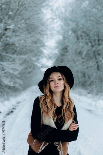 a young stylish woman in a black hat is walking in a winter snowy forest © Liudmyla