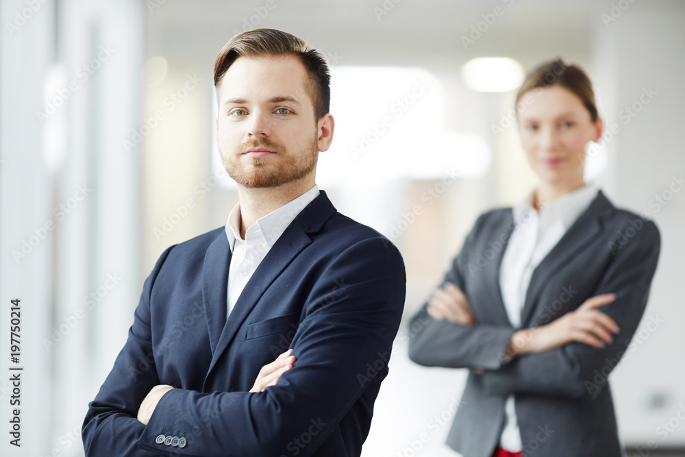 Cross-armed young businessman and his colleague in suits looking at camera Cross-armed young businessman and his colleague in suits looking at camera