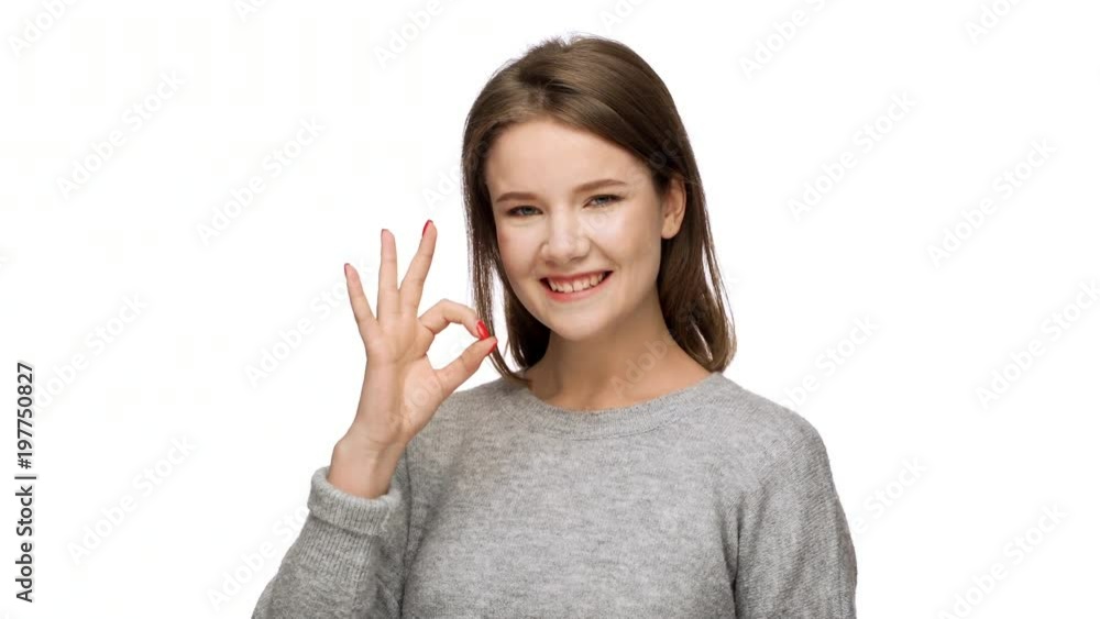 Portrait of joyous adult female 20s in casual clothing gesturing alright symbol with fingers with candid smile, over white background. Concept of emotions Portrait of joyous adult female 20s in casual clothing gesturing alright symbol with fingers with candid smile, over white background. Concept of emotions