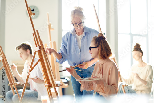 Young student and teacher of arts school discussing creative ideas of new painting at lesson