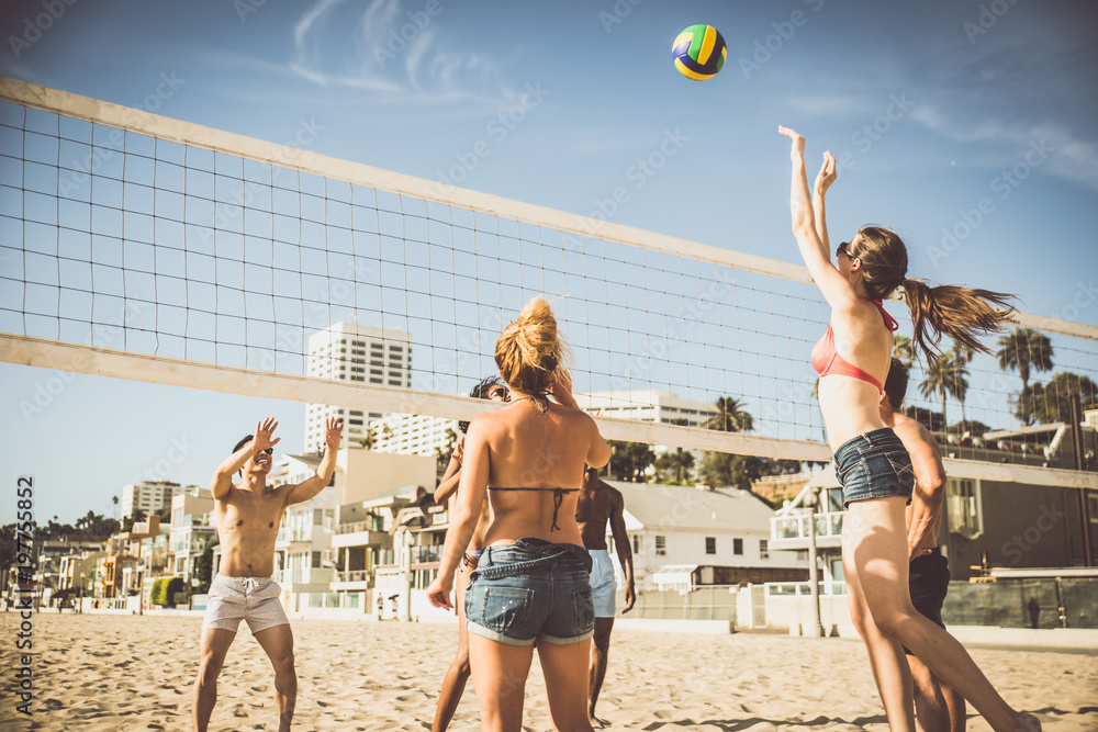 Obraz premium Grupa przyjaciół grających w siatkówkę plażową na plaży.