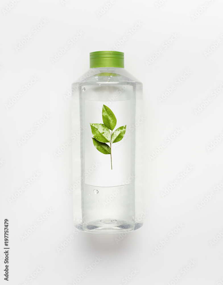 Transparent liquid bottle with green lid. Clean nature water with green leaves and branding mock up on white desk background , top view. Transparent liquid bottle with green lid. Clean nature water with green leaves and branding mock up on white desk background , top view.