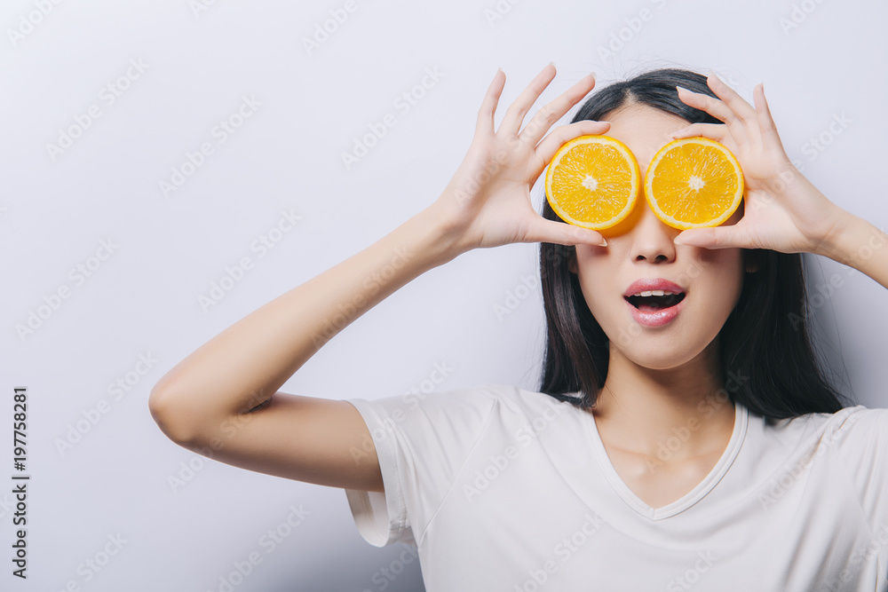 Studio portrait of young surprised happy asian girl holding two orange slices in t-shirt on white background and smiling. Fresh fruits and healthy diet concept. Free copy space provided Studio portrait of young surprised happy asian girl holding two orange slices in t-shirt on white background and smiling. Fresh fruits and healthy diet concept. Free copy space provided