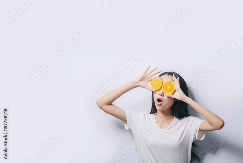 Studio portrait of young surprised funny girl holding two orange slices in t-shirt on white background and smiling. Fresh fruits and healthy diet concept. Free copy space provided