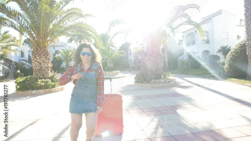 Summer lifestyle portrait of young woman posing with suitcase near resort photo