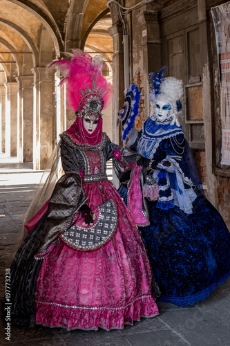 Two women in masks and ornate blue and pink costumes standing near the Rialto Market at Venice Carnival (Carnivale di Venezia)