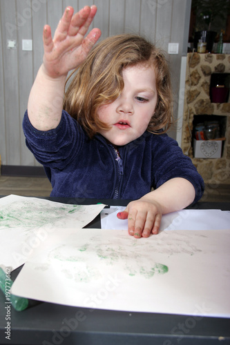 little blonde girl painting with her hands on a paper at home.