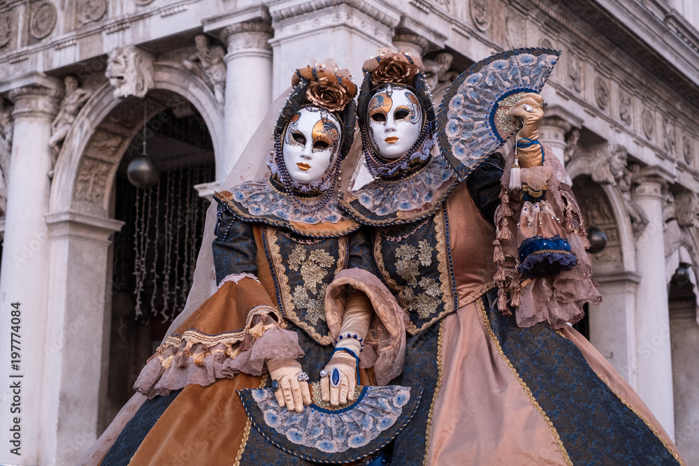 Obraz premium Two women in ornate costumes and painted masks, standing in St Marks Square during Venice Carnival (Carnivale di Venezia)
