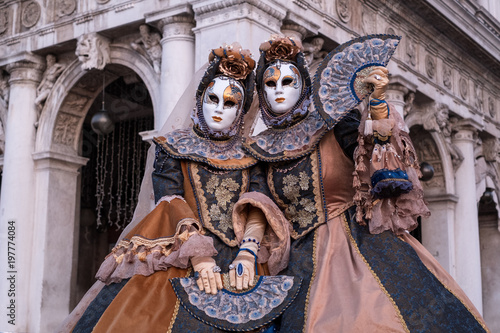 Two women in ornate costumes and painted masks, standing in St Marks Square during Venice Carnival (Carnivale di Venezia) © Lois GoBe
