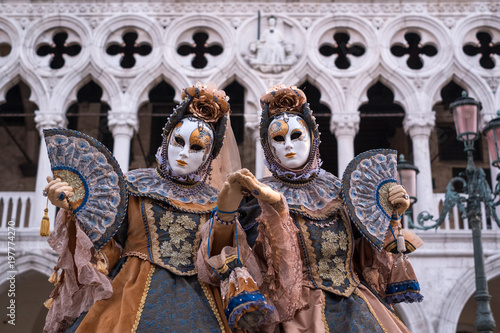 Two women in ornate costumes and painted masks, standing in St Marks Square during Venice Carnival (Carnivale di Venezia) © Lois GoBe