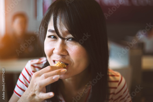 Asian woman eating fried chicken in a restaurant.