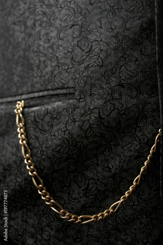 goldene Uhrenkette einer Taschenuhr hängt aus einer schwarzen Westentasche