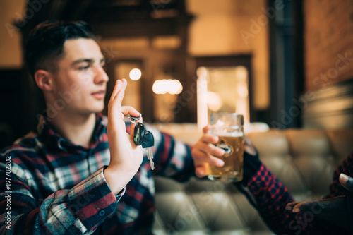 Do not drink and drive. Young guy is holding car keys and refusing to drink beer from his friend in pub