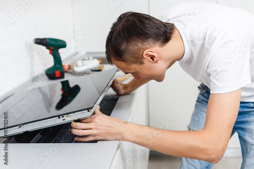 Young repairman installing induction cooker in kitchen