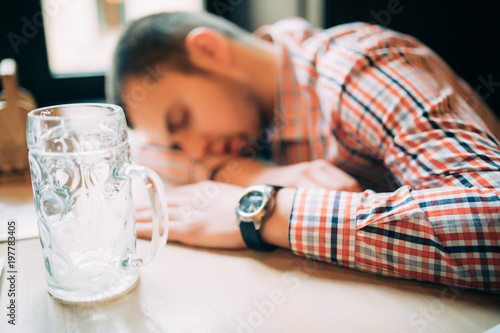 Drunk again. Drunk male customer leaning at the bar counter and sleeping while glass with beer standing near him