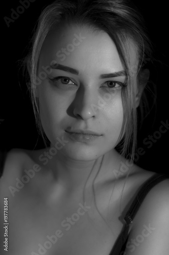 Black and white portrait pretty young woman in sweater on black background. Low key. Indoor.