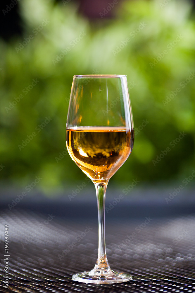 A glass of white wine or apple juice stands on a table in good light with a beautiful green background.