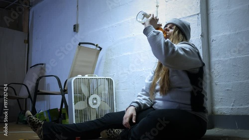 A Woman with an alchohol addiction drinks liquor in a trap house ALT photo