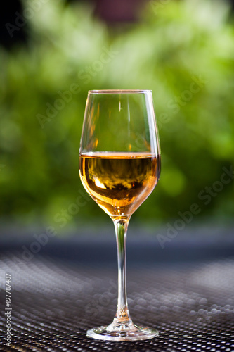 A glass of white wine or apple juice stands on a table in good light with a beautiful green background.