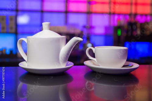 White teapot and tea cup on color lights background 