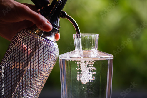 Photos The hand holding the siphon, bubbles with clear water in a glass decanter