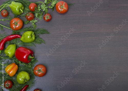Red tomato and green cucumber. Red and yellow peppers with garlic on a wooden background. Fresh vegetables lie on a wooden background.