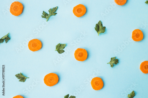 Bright round ringlets of carrots with green parsley sprigs on a blue background. Top view  flat lay