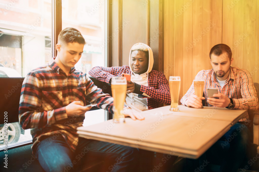 people, men, leisure, friendship and technology concept - Young men multiracial friends with smartphones drinking beer at bar or pub people, men, leisure, friendship and technology concept - Young men multiracial friends with smartphones drinking beer at bar or pub