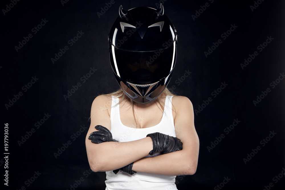 Isolated picture of unrecognizable muscular female in white tank top crossing arms on her chest while posing in studio wearing leather gloves and protective motorcycle helmet with black shield