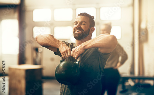 Smiling young man lifting a dumbbell while working out