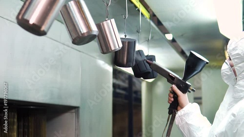 Powder coating of metal parts. A man in a protective suit sprays powder paint from a gun on metal products