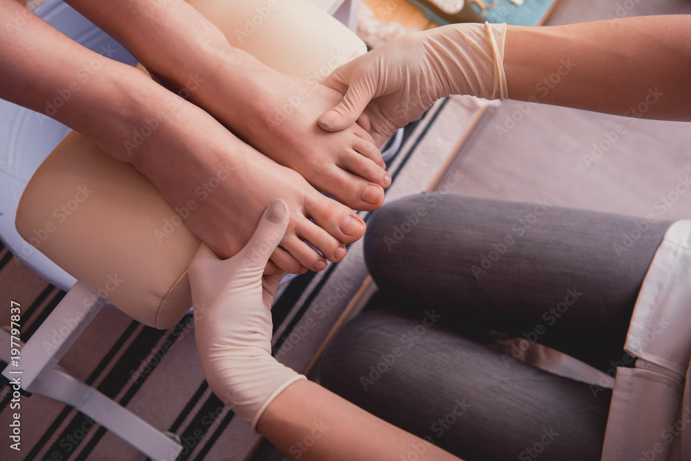 Obraz premium Top view close up woman hands in gloves holding feet of young woman. Treatment concept