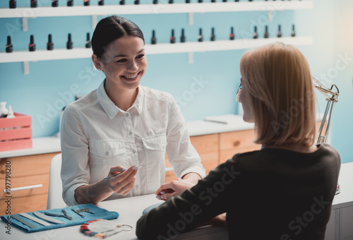 Cuadro en lienzo Happy woman manicurist talking with client while doing manicure for her
