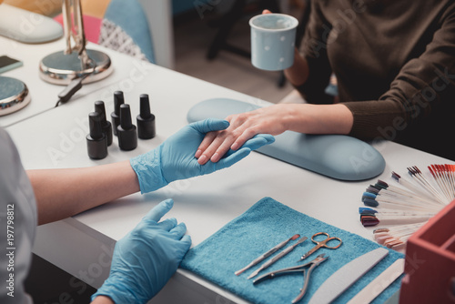 Close up nail artist hand doing nude manicure for client. They sitting at table. Beauty salon concept