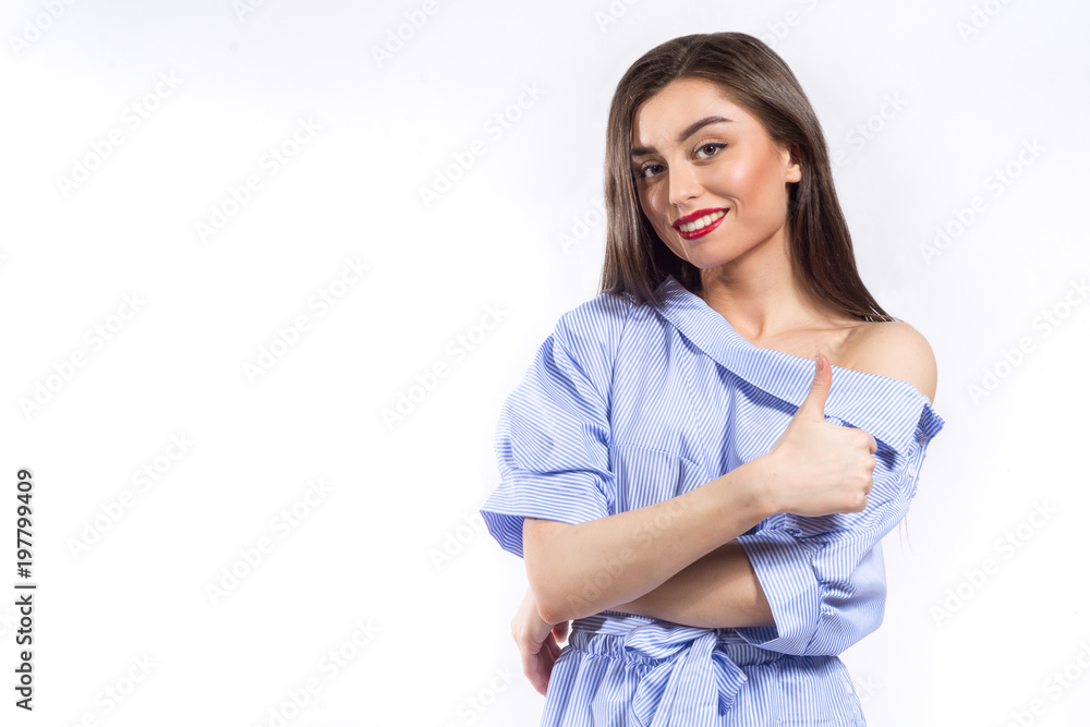 Young beautiful smiling woman striped blue and white dress shirt posing and showing thumb up over white background Young beautiful smiling woman striped blue and white dress shirt posing and showing thumb up over white background