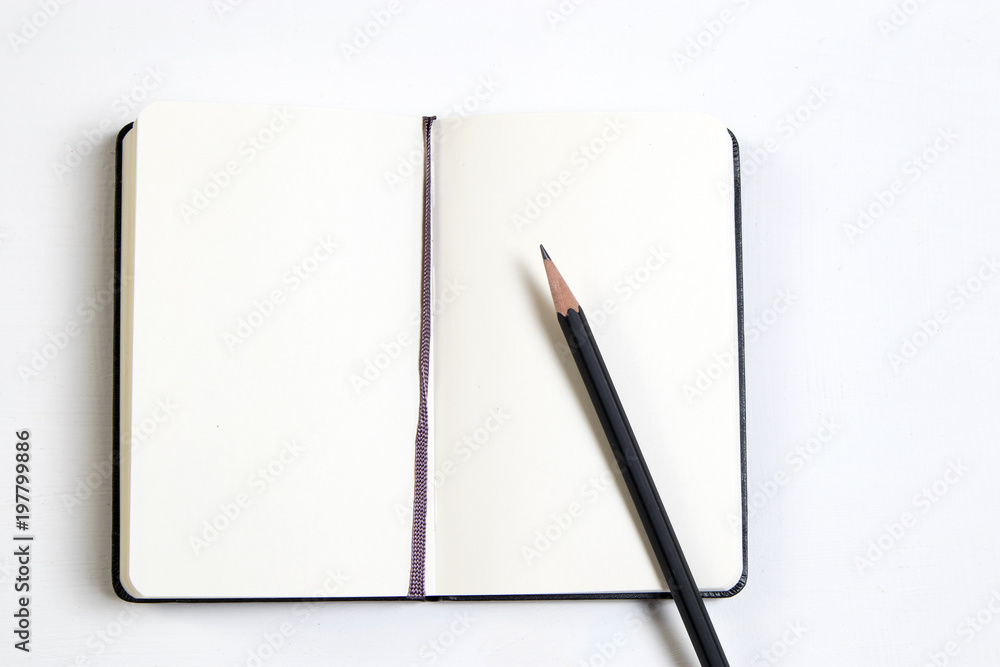 a white notebook and a black pencil on a white wooden table. a white notebook and a black pencil on a white wooden table.