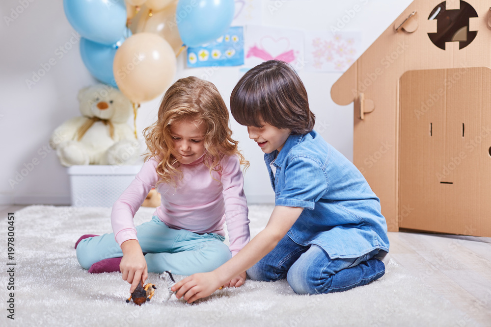 Little smiling girl and boy toying with figures animals in nice children room with balloons and small fairytale house Little smiling girl and boy toying with figures animals in nice children room with balloons and small fairytale house