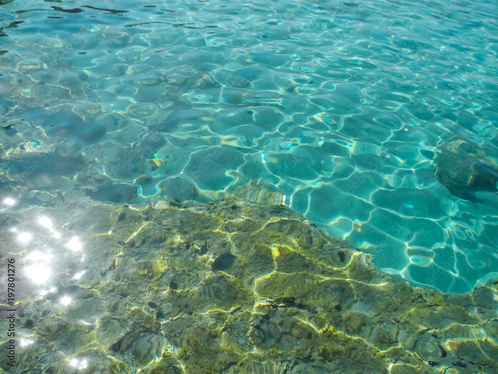 Crystal turquoise water with twinkling and reflecting sunlight and stones on seabed