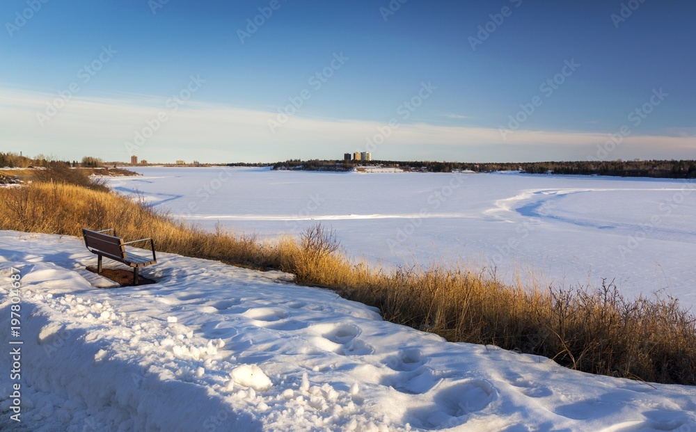 Isolated Park Bench and Distant Snowy Glenmore Reservoir Scenic Landscape in South Calgary Alberta on early Springtime Sunny Afternoon