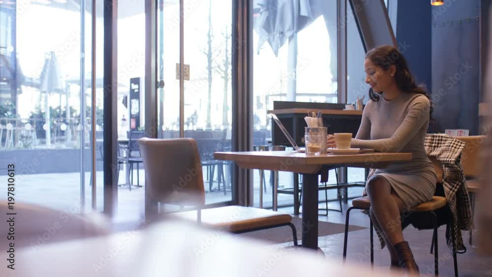 Lone female in a coffee shop working on her laptop one morning as a waiter brings her order Lone female in a coffee shop working on her laptop one morning as a waiter brings her order