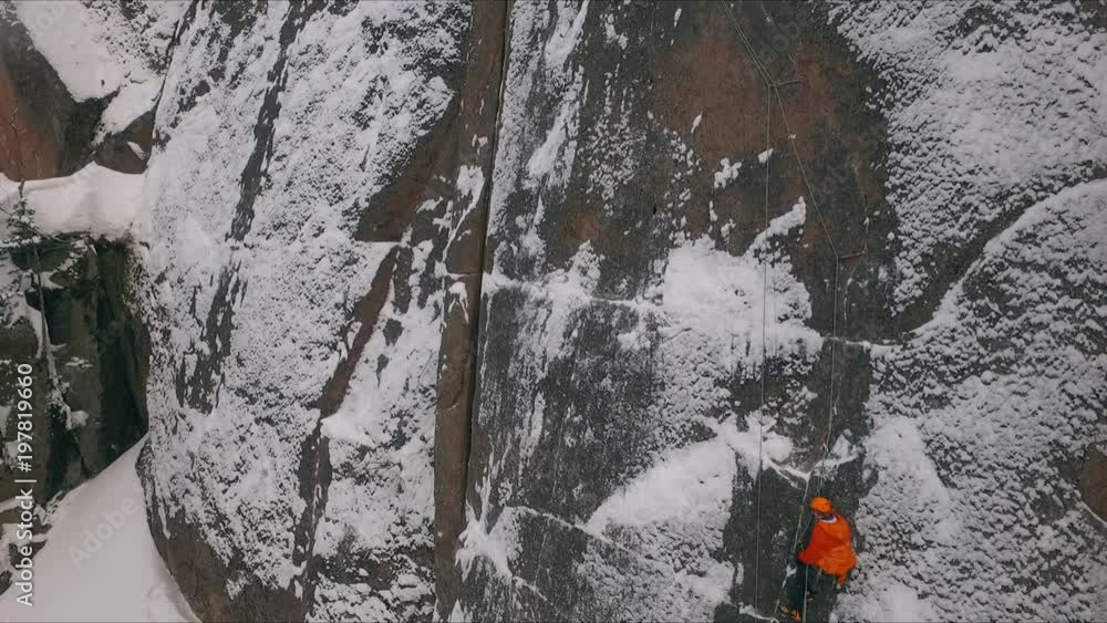 Aerial view of a rock climber climbing a steep cliffs during a sunny winter day. Aerial view of a rock climber climbing a steep cliffs during a sunny winter day.