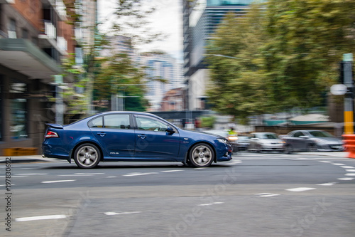 Blue car in motion on the road, Sydney, Australia. Car moving on the road, blurred buildings in background.