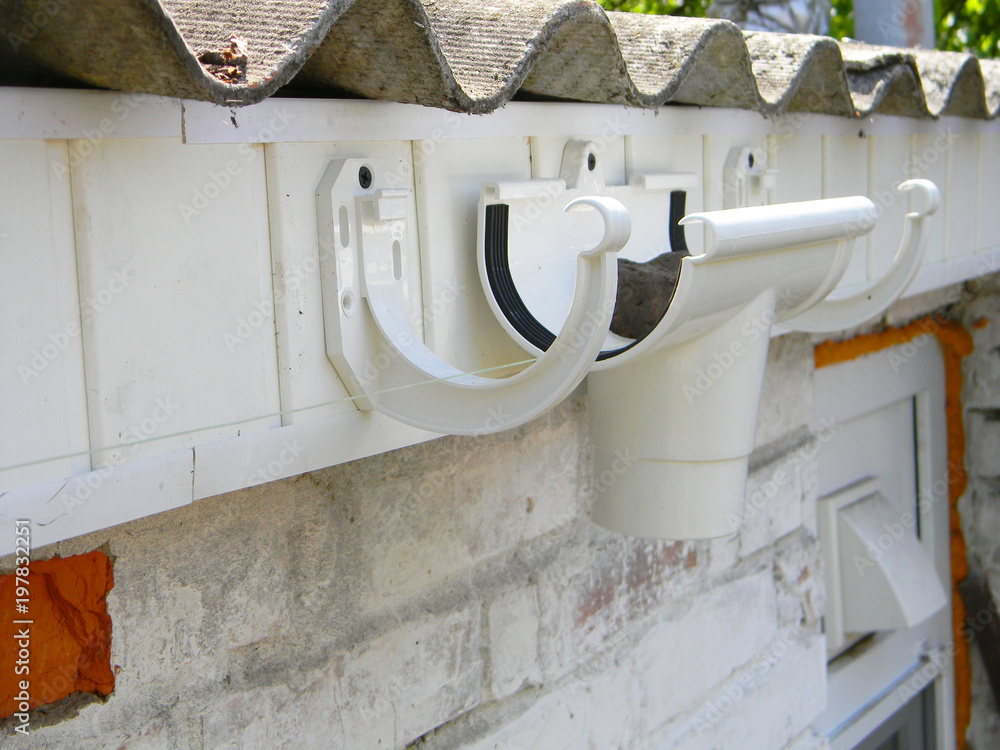 Installing plastic roof gutter holder for dowspout drain pipe. Plastic