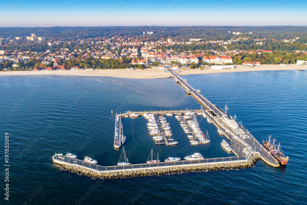 Fototapeta premium Sopot resort in Poland. Wooden pier (molo) with marina, yachts, pirate tourist ship, beach, vacation infrastructure, hotels, park and promenade. Aerial view at sunrise.